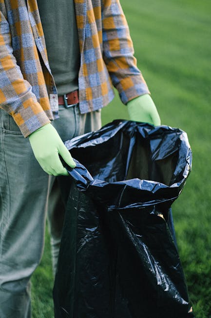 Close-up view of a black plastic rubbish bag with a tightly knotted top, sitting on or next to other similar black bags. The bags are made of shiny, crinkled plastic material and appear to be filled w